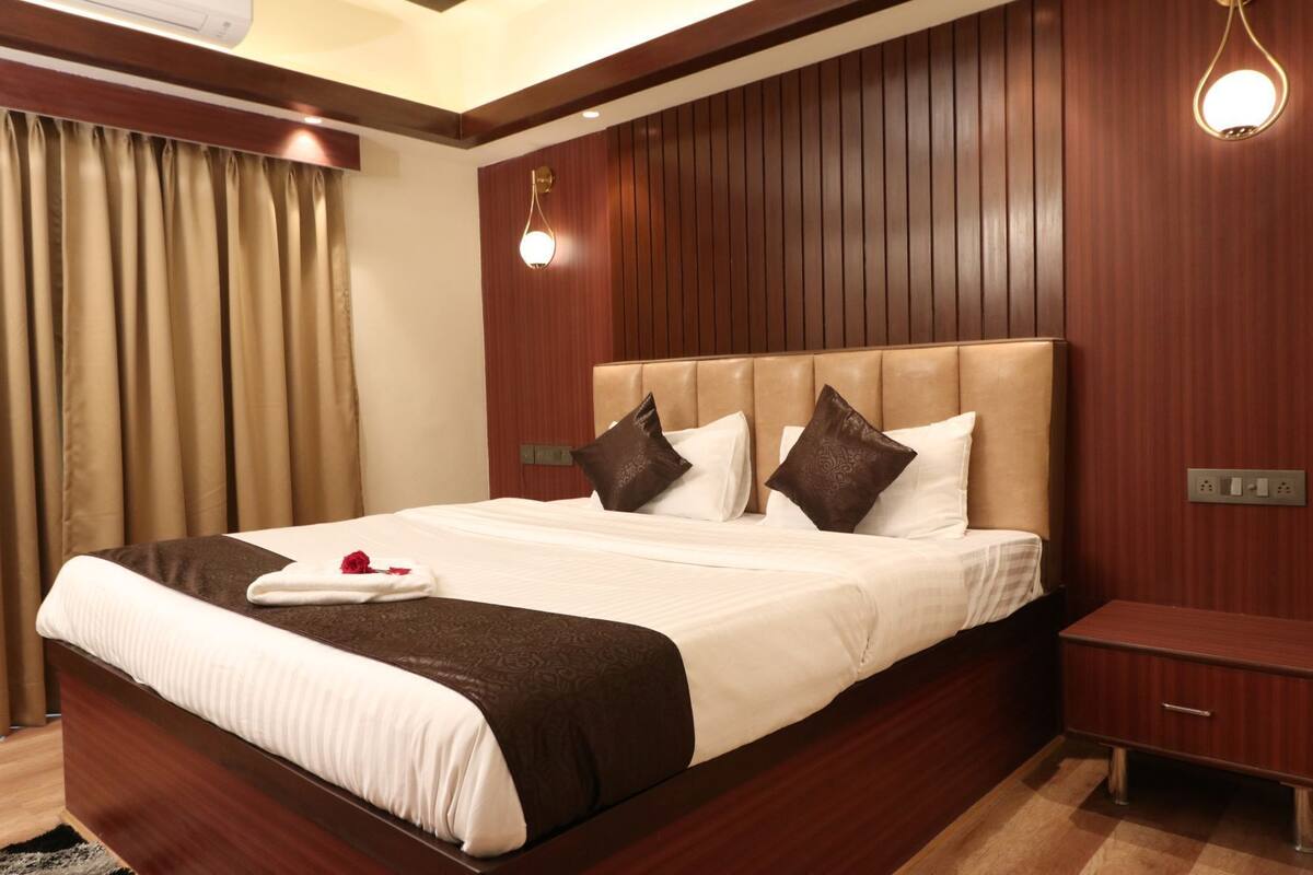 A hotel room with a large bed, wooden panel walls, a nightstand, and a wall-mounted light fixture.
