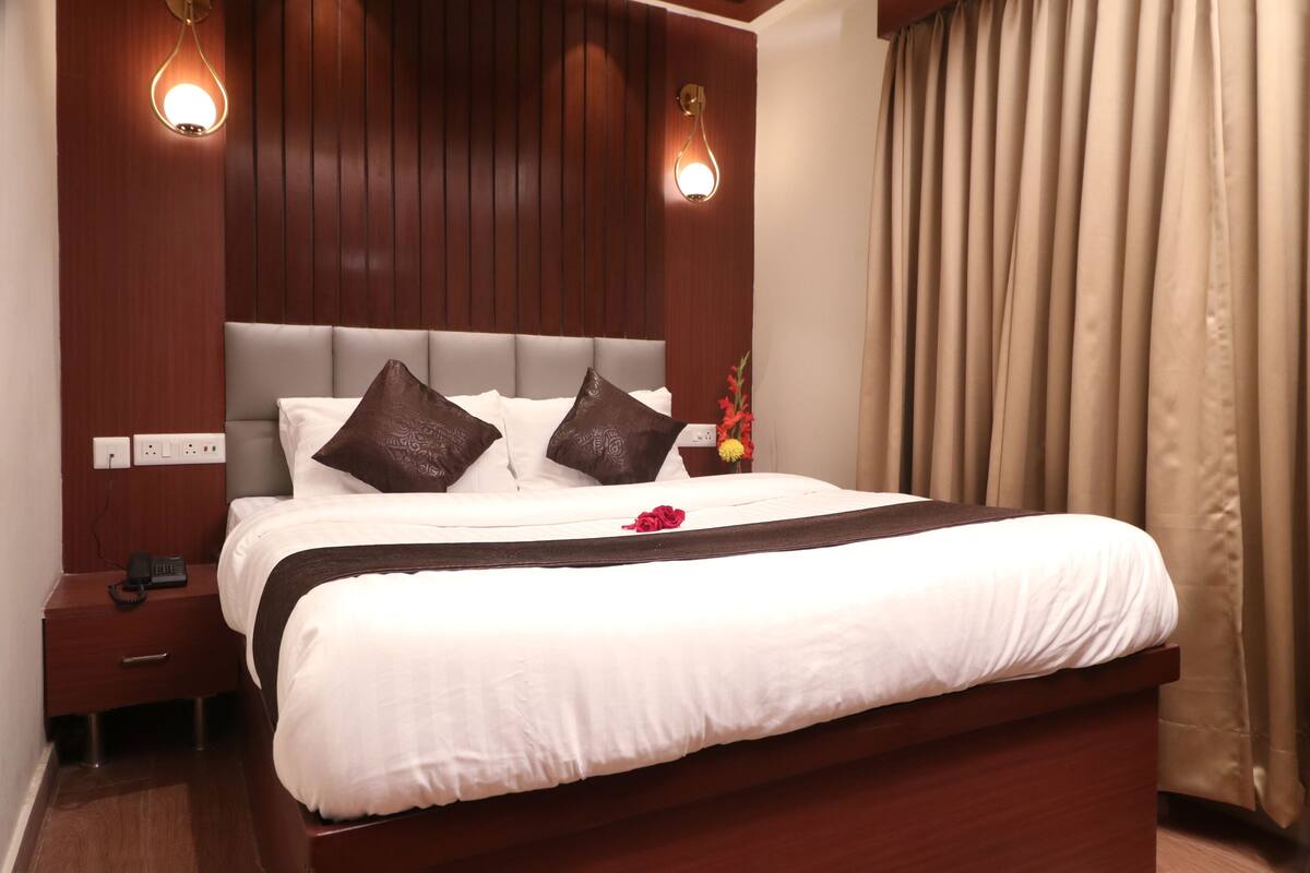 A neatly made bed with a white comforter and brown pillows, a wooden headboard, and a bedside table with a phone and a lamp.