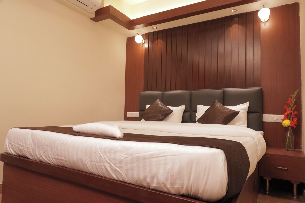 A hotel room with a large bed, wooden headboard, and a nightstand with a vase of flowers.