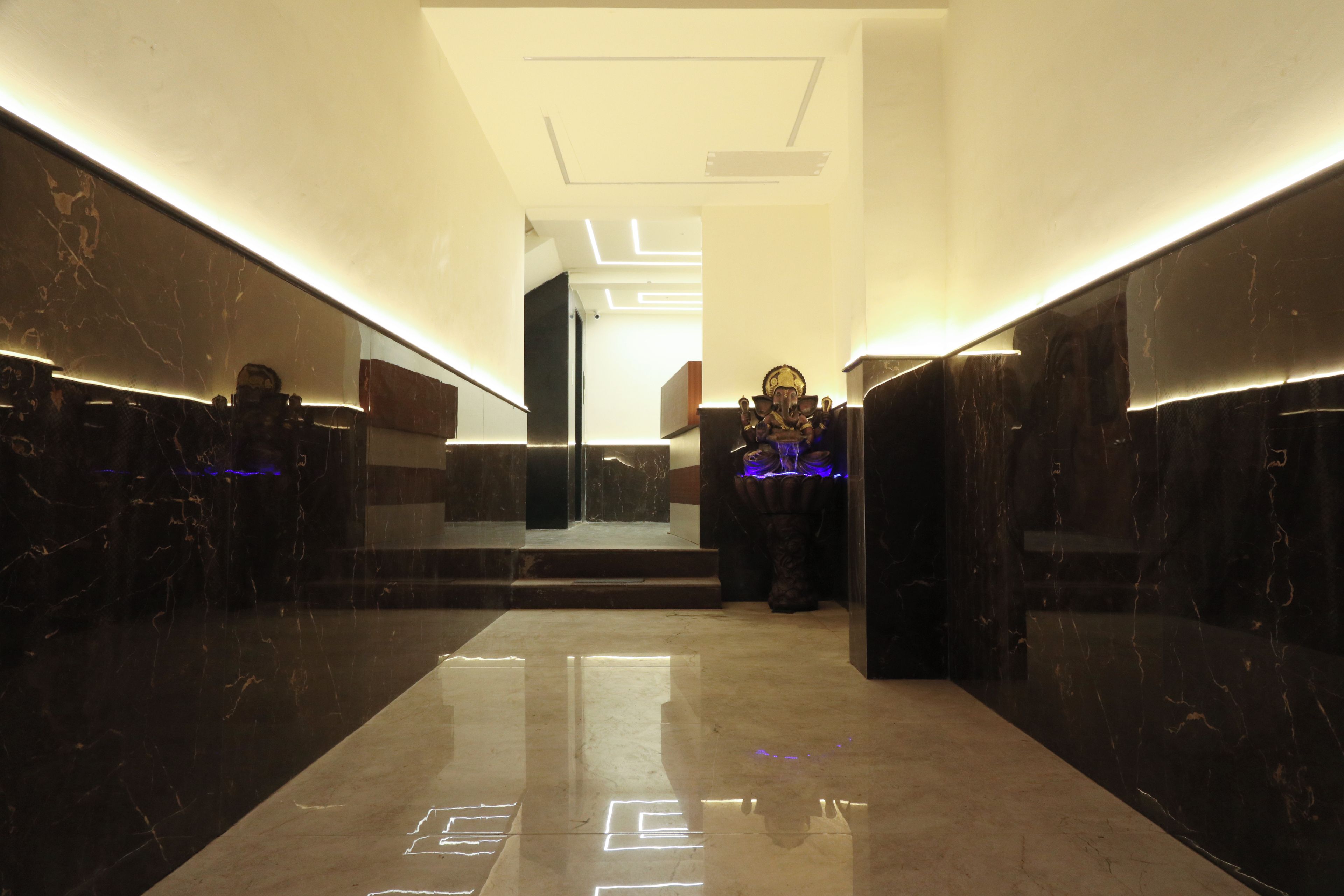A modern hallway with marble walls and a reflective floor, leading to a staircase.