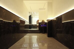 A modern hallway with marble walls and a reflective floor, leading to a staircase. - The Lake Hotel (Kolkata)