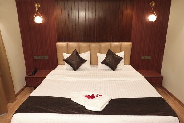 A hotel room with a large bed, wooden headboard, two bedside tables, and a telephone on one table. - The Lake Hotel (Kolkata)