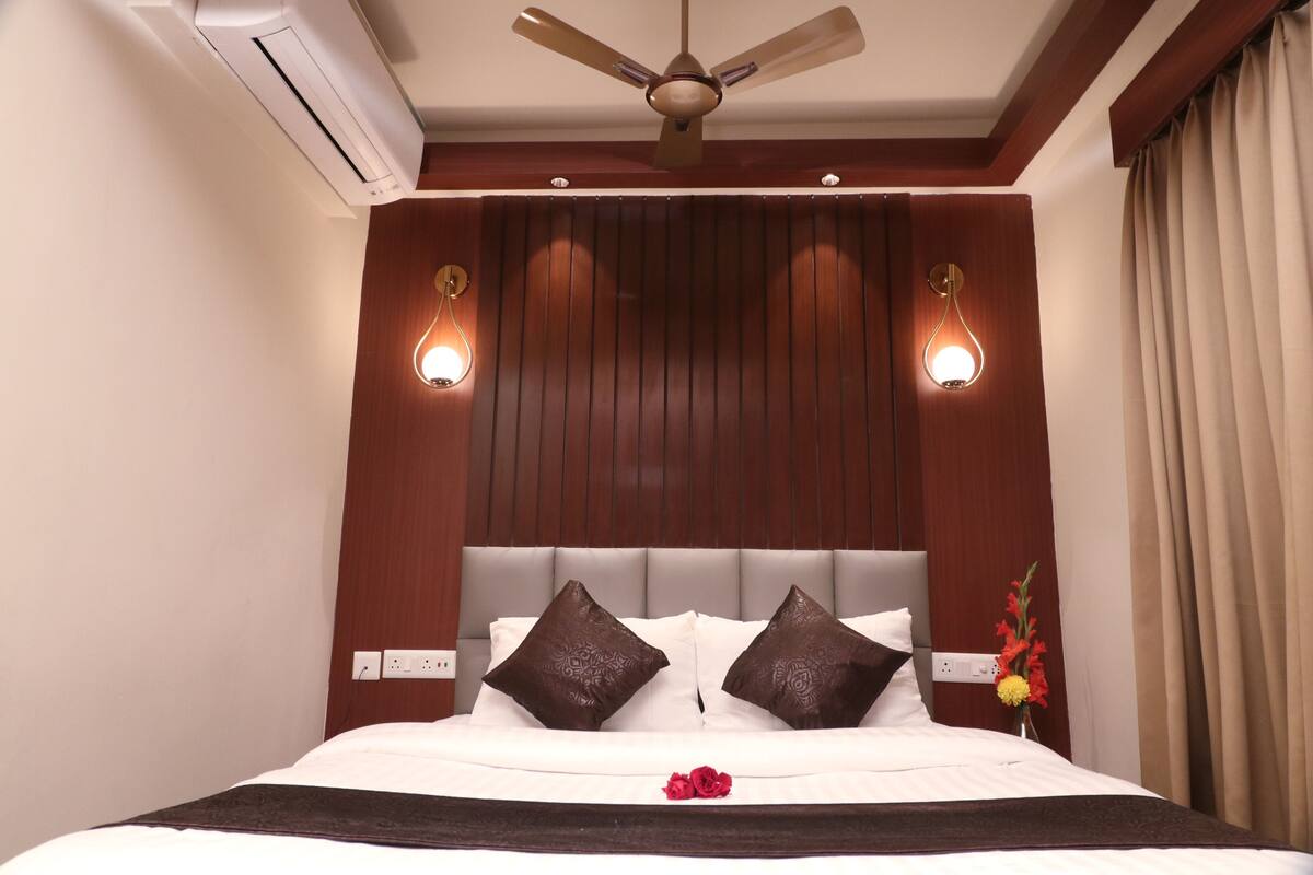 A hotel room with a large bed, a ceiling fan, wall-mounted lights, and a power outlet.