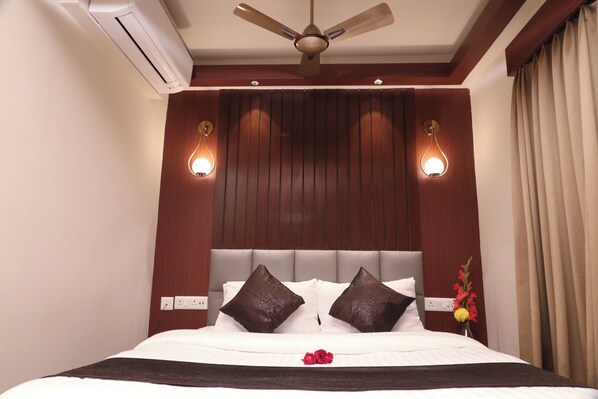 A hotel room with a large bed, a ceiling fan, wall-mounted lights, and a power outlet. - The Lake Hotel (Kolkata)