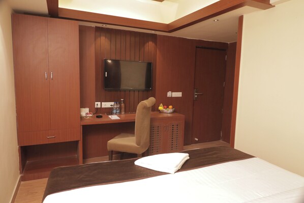 A hotel room with a bed, a desk, a chair, a television, and a wardrobe. - The Lake Hotel (Kolkata)