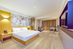 Une chambre d’hôtel avec un grand lit, des tables de chevet, un bureau, une chaise, une télévision et un mur orné d’une fresque représentant un paysage urbain.
