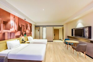 Une chambre d’hôtel avec deux lits, une télévision, une petite table avec des chaises et une fresque représentant un paysage urbain sur le mur.