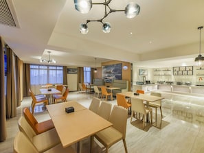 Une salle à manger d’hôtel avec des tables et des chaises, une cuisine en arrière-plan et un grand tableau accroché au mur.