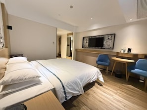 Habitación de hotel con una cama, un escritorio, dos sillas, un televisor y una obra de arte en la pared.