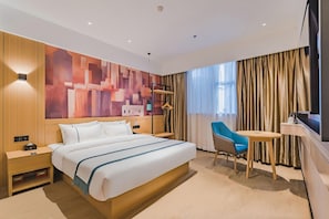 A modern hotel room with a large bed, a desk, a chair, and a television.