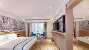 Ett hotellrum med en stor säng, två stolar, en tv och en väggmålning som föreställer en stadsbild.