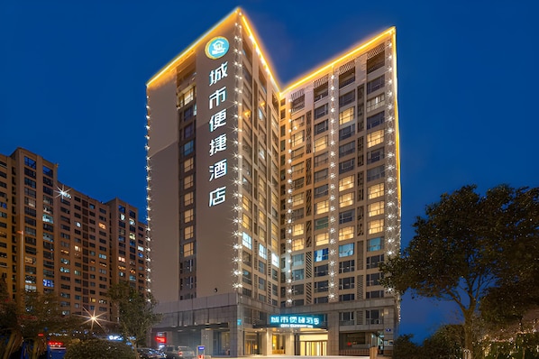 Un edificio hotelero de varios pisos con señalización iluminada, una entrada destacada y una vista despejada del entorno urbano.