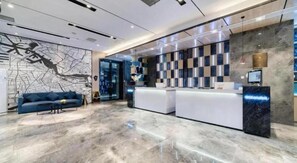 A modern hotel lobby with a reception desk, seating area, and a large wall map.