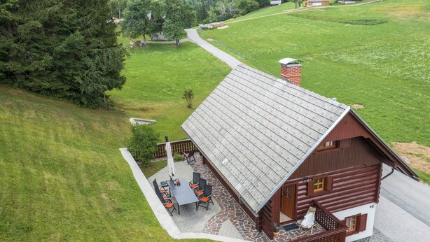 Eine Blockhütte mit Terrasse, umgeben von einer grünen Landschaft und Bäumen.