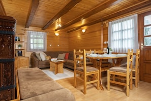 A cozy cabin interior with a wooden dining table, chairs, a sofa, and a wooden cabinet.