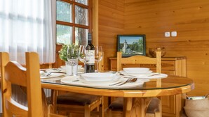 Ein Essbereich in einer Holzhütte mit einem runden Glastisch, gedeckt für vier Personen, umgeben von Holzstühlen.