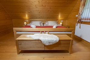A wooden cabin room with a bed, bedside lamps, a wooden table, and a white fur throw.