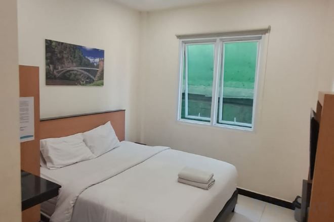 A bedroom with a bed, a window, and a painting on the wall.