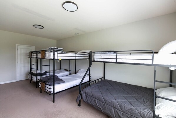 A bunk bed room with a door, carpeted floor, and a ceiling light fixture.