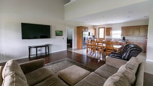 A spacious living room with a large flat-screen TV, a dining area with wooden furniture, and a kitchen with wooden cabinets.