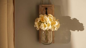 A rustic wooden lantern with a glass jar containing white flowers, hanging on a wall.