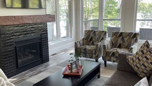 A modern living room with a fireplace, comfortable seating, and large windows offering a view of the outdoors.