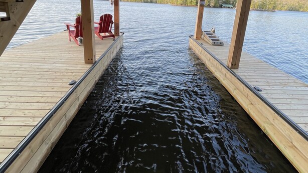 A wooden dock extending over a body of water with a covered seating area and red chairs.