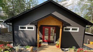 A modern cabin with a red door, wooden deck, and potted plants.