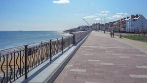 A seaside promenade with a brick walkway, metal railing, and residential buildings in the background. - Crown Apartments 3A - UK3380 (Newcastle upon Tyne)