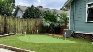 Um quintal com campo de putting, cerca de madeira e uma palmeira.