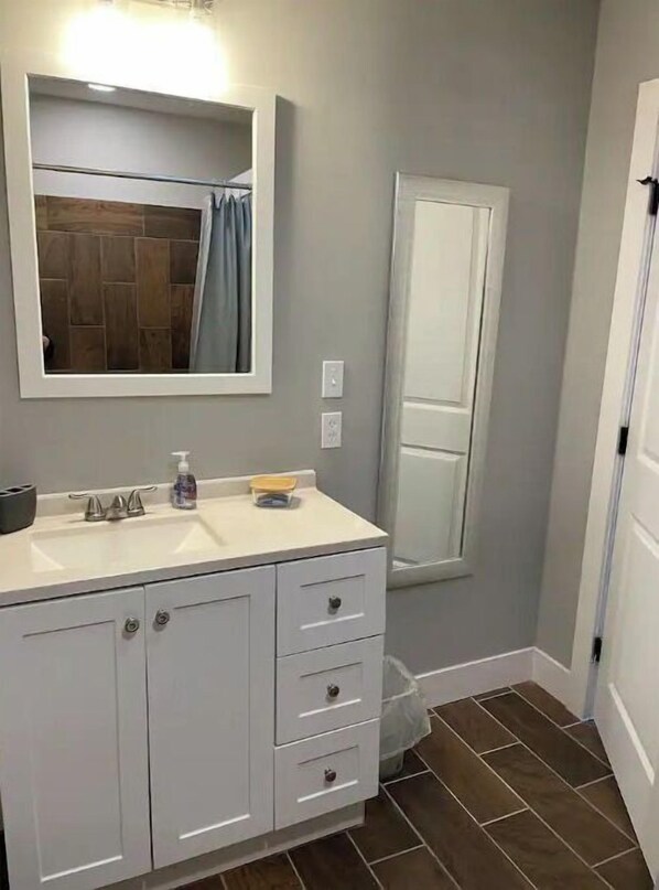 A bathroom with a white vanity, a mirror, a towel rack, and a shower curtain.