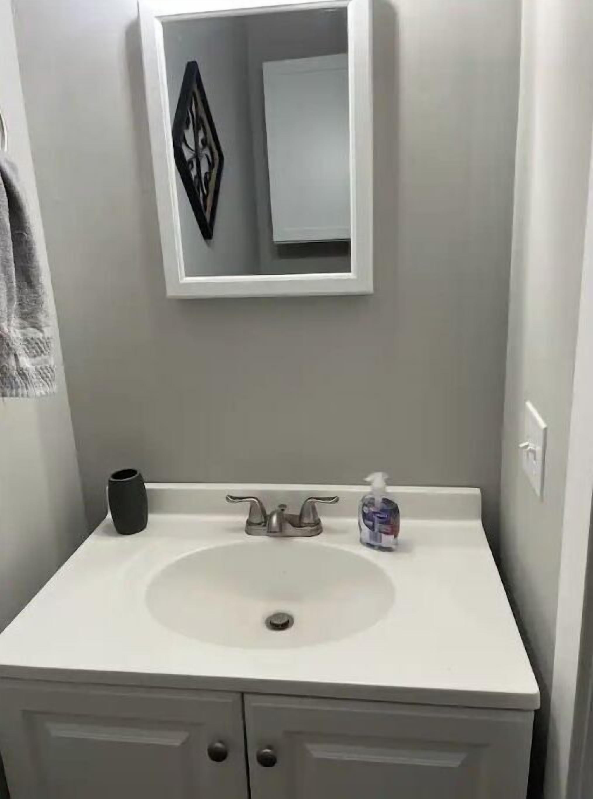 Un baño con un lavabo blanco, un espejo, un jarrón negro y un dispensador de jabón.