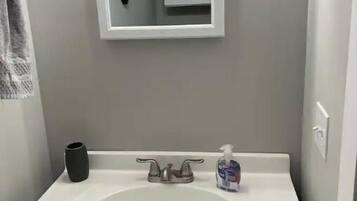 Un baño con un lavabo blanco, un espejo, un jarrón negro y un dispensador de jabón.