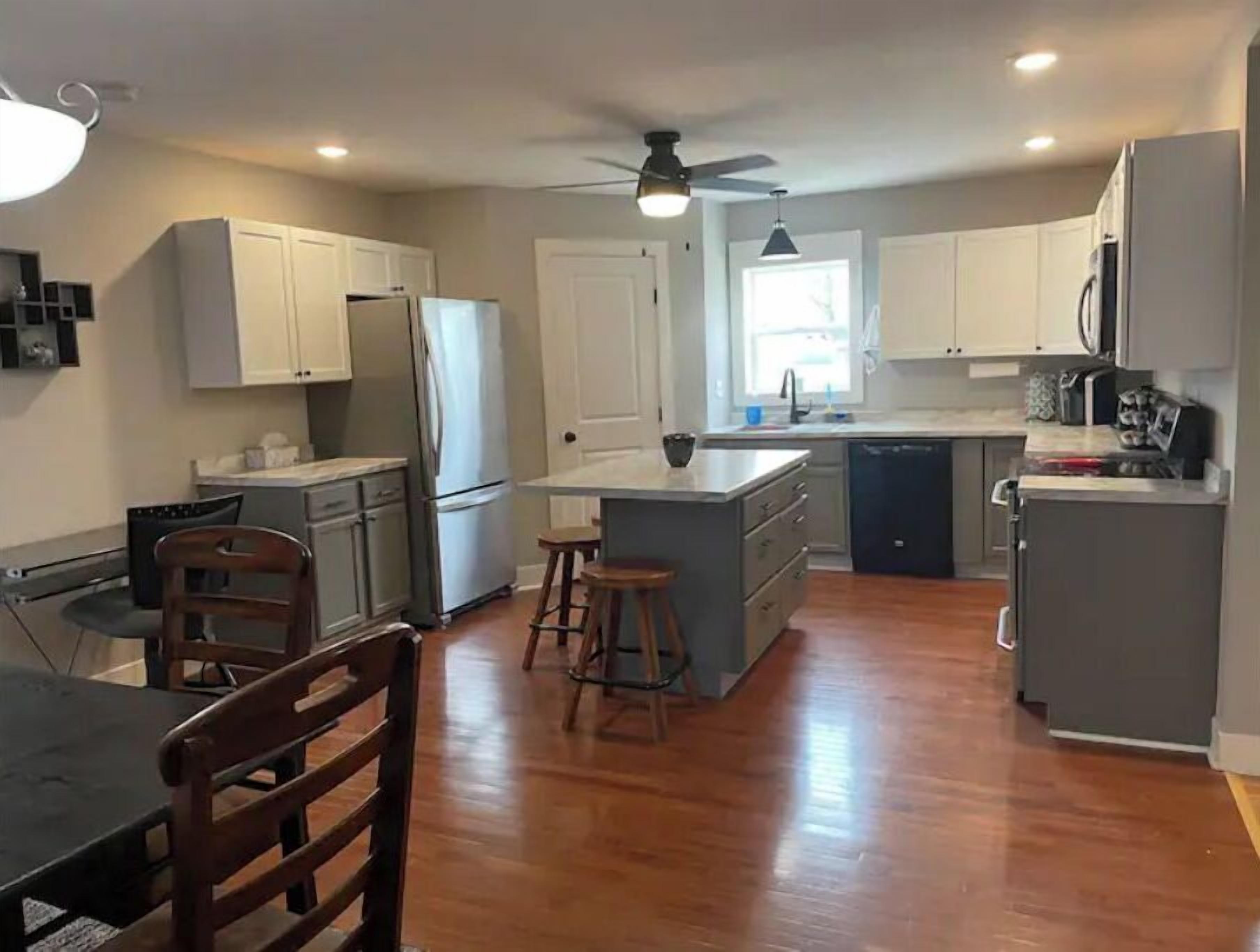 A modern kitchen with white cabinets, a stainless steel refrigerator, a dishwasher, and a bar stool.