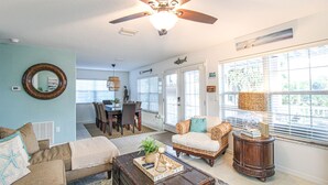 A living room with a ceiling fan, a dining area with a table and chairs, and a view through large windows. - Luxury Beach House, Private Salt Pool. Walk to the Beach (Palm Coast)
