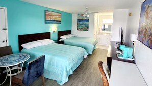 A hotel room with two beds, a small table, a chair, a TV, and artwork on the walls.