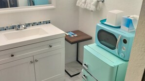 A bathroom with a white sink, a mirror, a small table with a towel, and a vintage blue microwave.