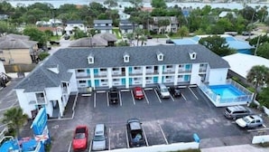 A motel with a swimming pool, multiple parking spaces, and a view of the surrounding area.