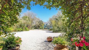 A gravel pathway leading to a house surrounded by lush greenery and potted plants.