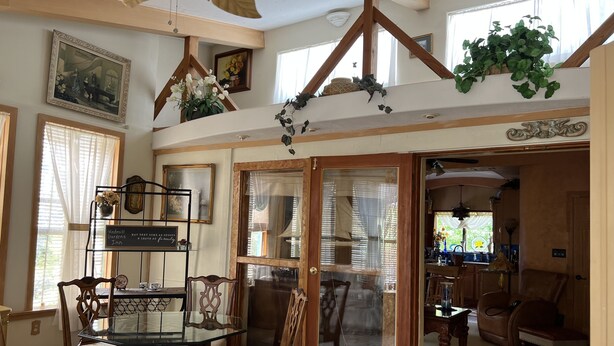 A dining area with a glass table and wooden chairs, a staircase with wooden railings, and a large window with curtains.