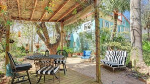 A covered outdoor seating area with a wooden deck, metal chairs, and a striped sofa.