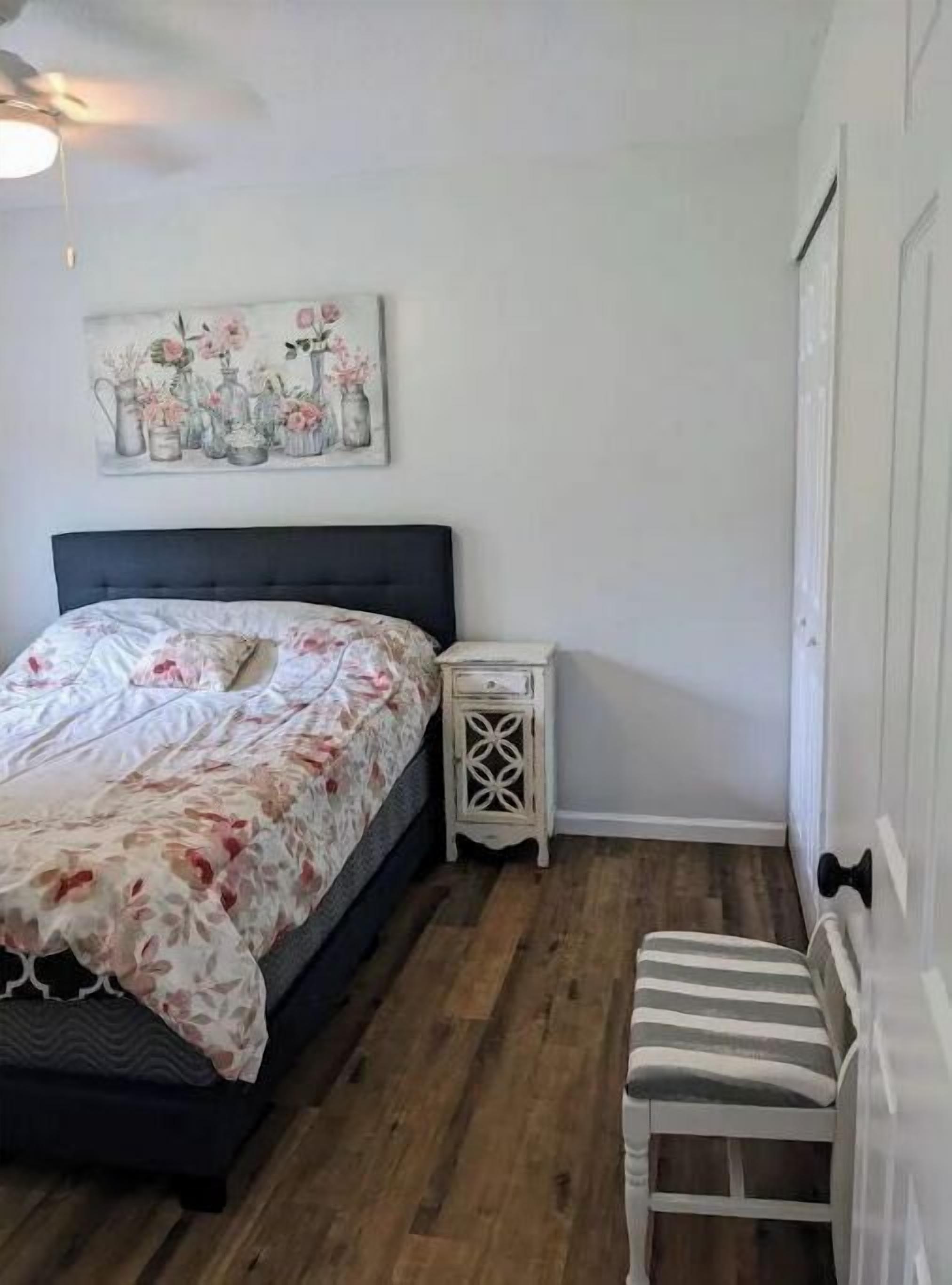 A bedroom with a bed, a nightstand, a chair, and a wall-mounted painting.