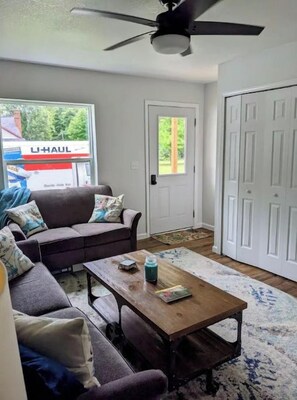 A living room with a sofa, coffee table, and a U+HAUL sign visible through the window. - 3 Bedroom 5 Minutes from Torch Lake/15 From Shanty Creek/30 From Boyne (Central Lake)