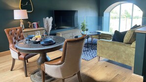 Ein modernes Wohnzimmer mit einem runden Esstisch, Ledersesseln, einer Couch, einem Fernseher und einem großen Fenster.