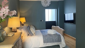Ein Schlafzimmer mit einem Bett, Nachttischlampen, einem Fernseher, einem Fenster und einer Zimmerpflanze.