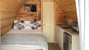 Quarto de sótão acolhedor com cama, almofadas, um quadro, uma kitchenette pequena e uma porta.