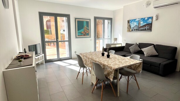 Un soggiorno moderno con zona pranzo, caratterizzato da un tavolo grande, un divano e un angolo cottura.
