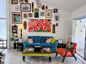Un salon avec un canapé bleu, une table basse et un fauteuil à motifs tropicaux.