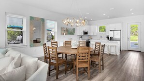 A modern kitchen with white cabinets, a central island, and a dining area with wooden chairs and a round table. - Bliss: Gated! Pool! Free Golf Cart! Sleeps 20! (Miramar Beach)