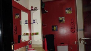 Un baño con pared roja, lavamanos blanco, inodoro y espejo.